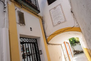 Eine schmale Straße mit einem weißen Gebäude, das eine gelbe Fassade, ein Metallgitter und eine dekorative Wandplakette hat.