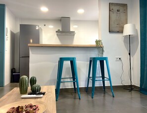 A modern kitchen with a built-in oven, a stainless steel refrigerator, and a wooden countertop. There are two blue stools and a cactus on the counter. - Casa Toril & Esparto de la Corredera (Cordoba)