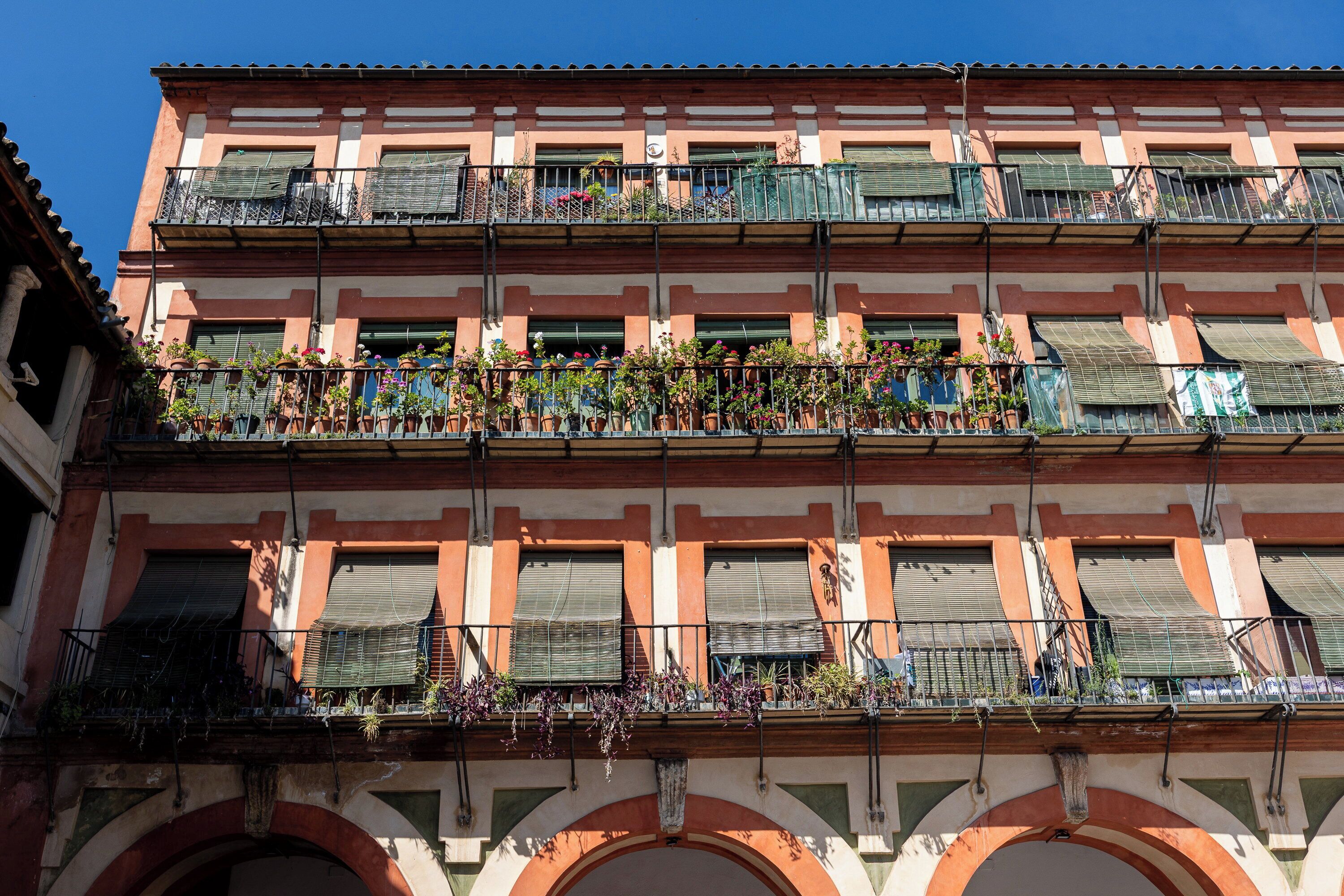 A multi-story building with balconies, some with plants and flowers.