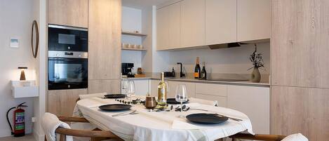 A modern kitchen with a dining table set for two, equipped with a coffee machine, wine bottles, and a decorative vase.