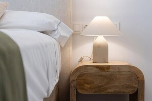 Ein Bett mit weißer Bettwäsche und ein Nachttisch aus Holz mit einer Lampe.