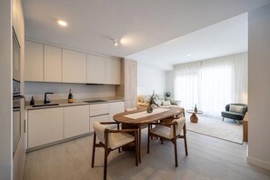 A modern kitchen with white cabinetry, a dining table with chairs, and a living area with a sofa and a coffee table. - PAR 00 Golf Estepona (Estepona)