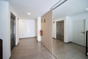 A hallway with a fire extinguisher mounted on the wall, doors, and a wooden panel divider. - PAR 00 Golf Estepona (Estepona)