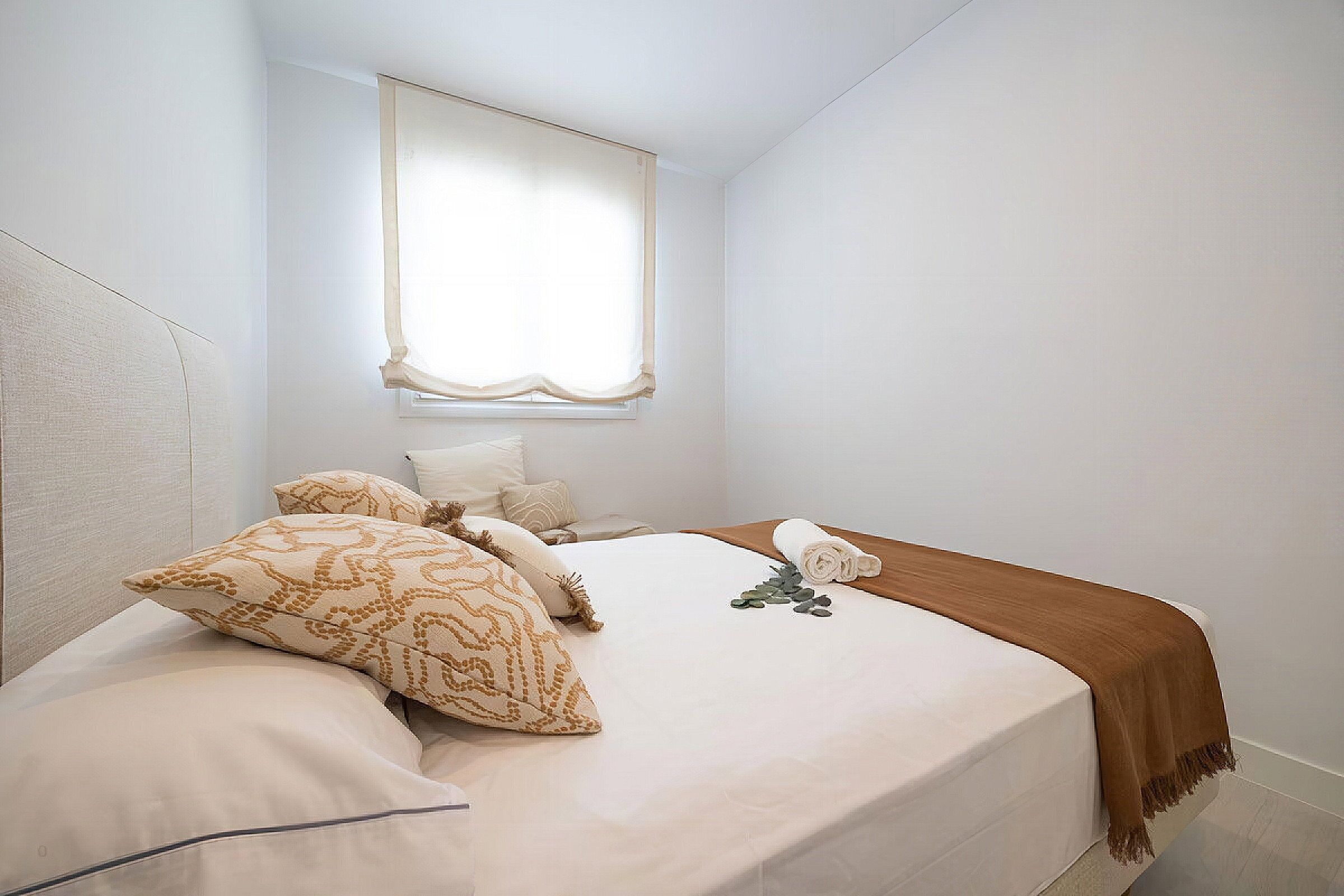 A bedroom with a bed, pillows, a window with a curtain, and a wooden headboard.