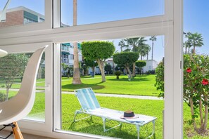 A room with a large window overlooking a well-maintained lawn with a lounge chair and a hat. - Luxury White Summer Benalmadena (Benalmadena)