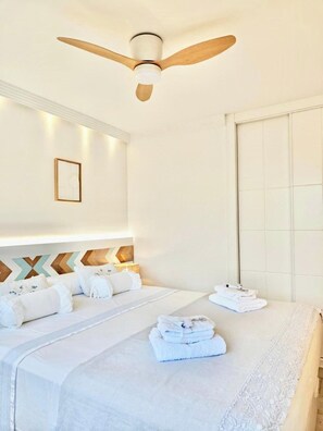 A hotel room with a bed, a ceiling fan, a wall-mounted picture frame, and a set of towels. - Luxury White Summer Benalmadena (Benalmadena)