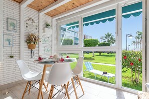 A dining area with a table set for two, white chairs, and a view of a well-maintained garden through large windows. - Luxury White Summer Benalmadena (Benalmadena)
