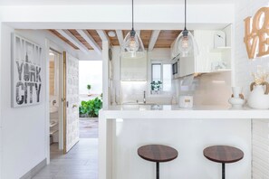 A modern kitchen with pendant lights, a white island with stools, and a view of the cityscape through the open door. - Luxury White Summer Benalmadena (Benalmadena)