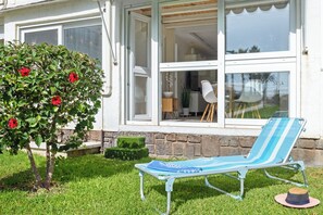 Een huis met een tuin, een blauw-witte ligstoel en een hibiscustak.
