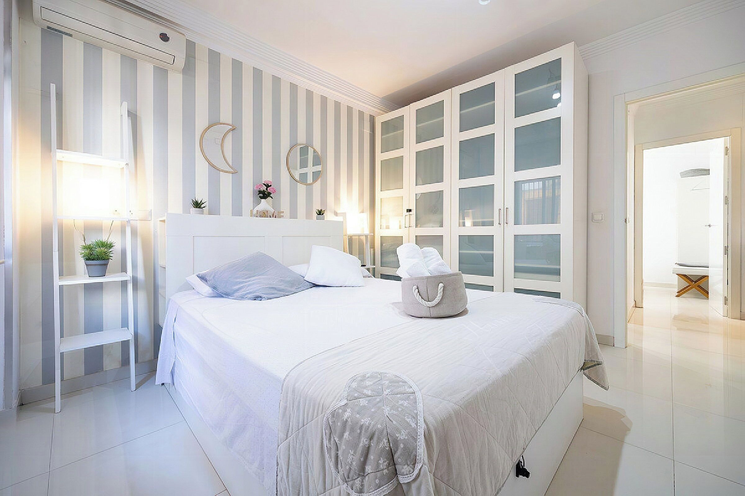 Une chambre à coucher avec un grand lit, une table de chevet, une commode, une armoire aux portes en verre et un miroir au mur.