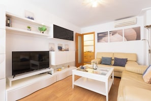 Ein modernes Wohnzimmer mit Fernseher, weißen Möbeln, einer Holztür und einem beigefarbenen Sofa.