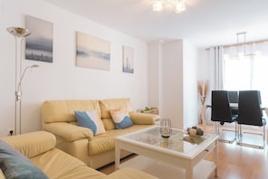 A living room with a beige sofa, a glass coffee table, and a dining area with black chairs. - Tradiciones marineras, la Jabega del Palo (Málaga)