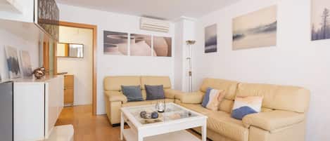 A modern living room with a beige sofa, a white coffee table, and a flat-screen TV.