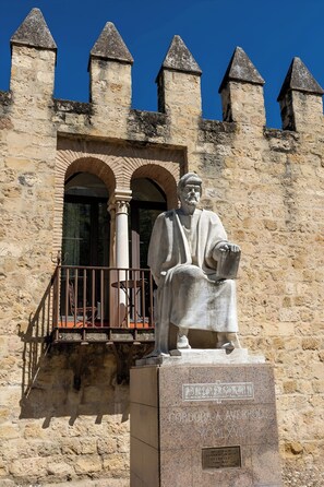 A stone building with a statue of a seated figure, a balcony, and a plaque with text. - Alcázares Apartment in Historic Center Córdoba (Cordoba)