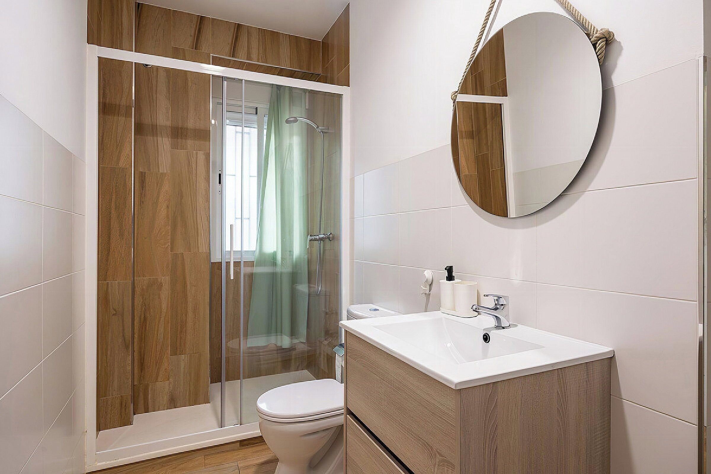 Un baño moderno con ducha envuelta en vidrio, lavamanos blanco y tocador de madera.