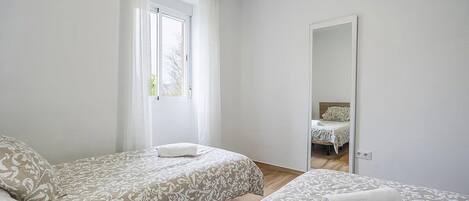 A bedroom with two beds, a window with curtains, a mirror, and a door.