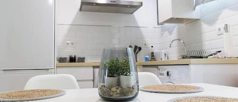 Una cocina moderna con electrodomésticos blancos, una mesa de vidrio con un centro de mesa de planta y un diseño limpio y minimalista.