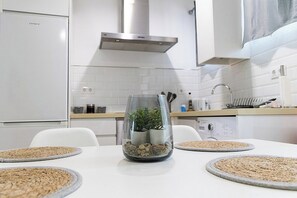A modern kitchen with white appliances, a glass-top table with a plant centerpiece, and a clean, minimalist design. - Calahorra Experience · Mezquita Frontline (Cordoba)