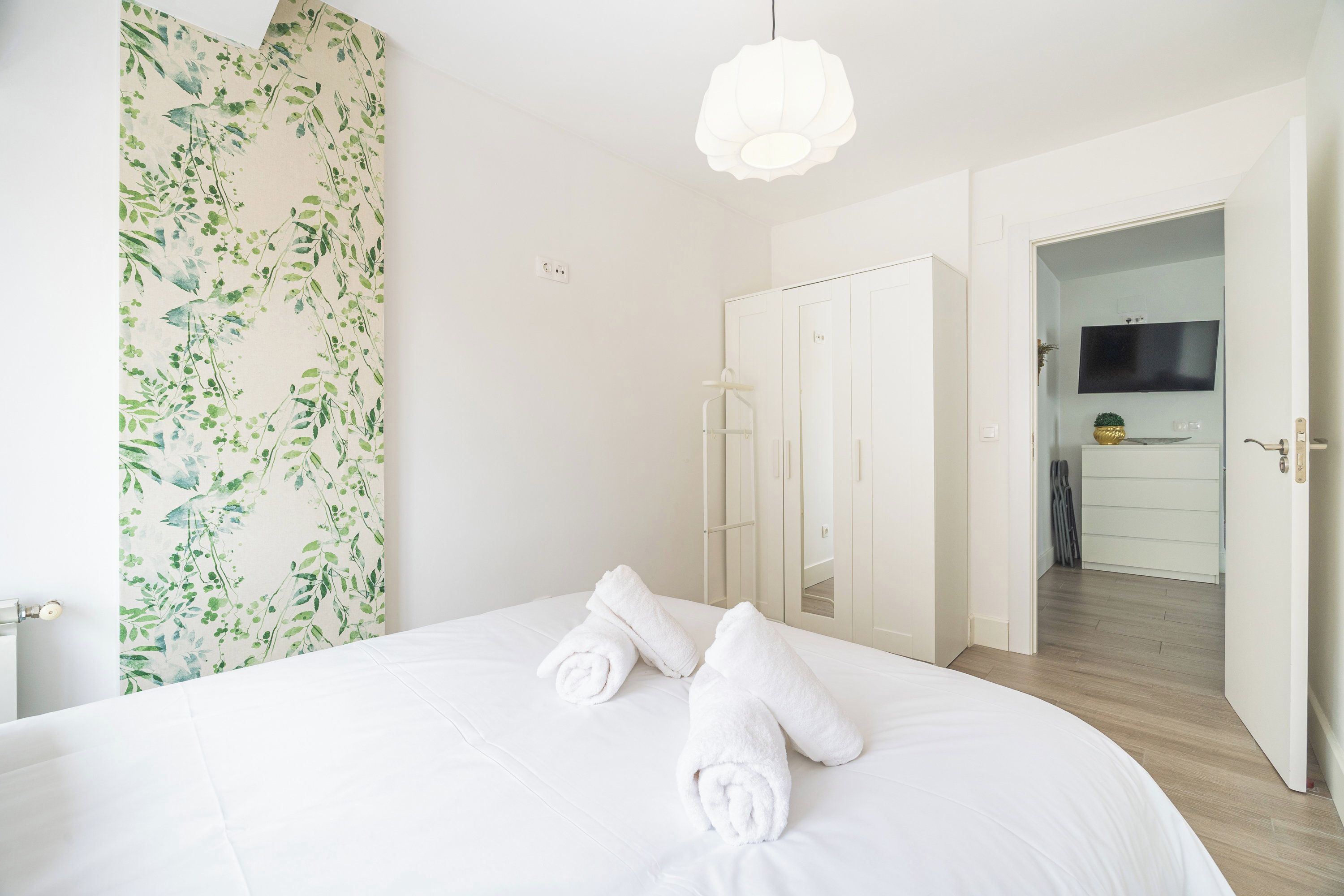 A hotel room with a bed, white towels, a wardrobe, a television, and a bathroom visible through an open door.