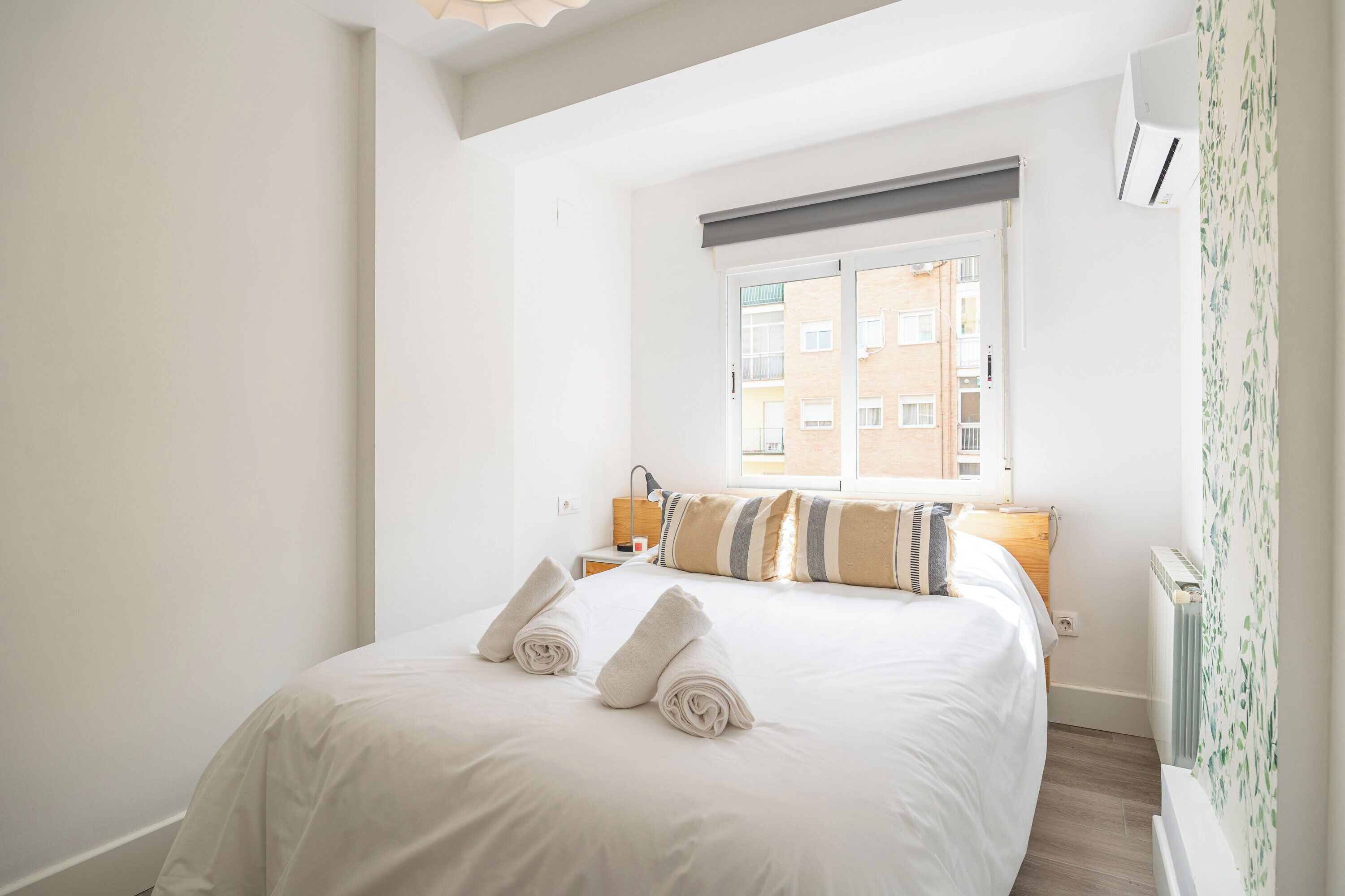 Una habitación de hotel con una cama, una mesita de noche, una lámpara, un ventanal y un radiador.