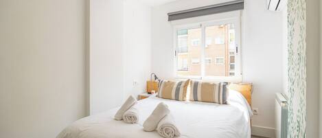 Una habitación de hotel con una cama, una mesita de noche, una lámpara, un ventanal y un radiador.