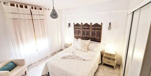 A bedroom with a bed, a nightstand, a lamp, and a chair. - Las vides de moriles (Cordoba)