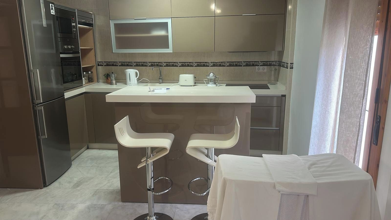 Een moderne keuken met roestvrijstalen apparatuur, een wit aanrecht en twee barkrukken.