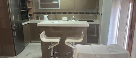 A modern kitchen with stainless steel appliances, a white countertop, and two bar stools.
