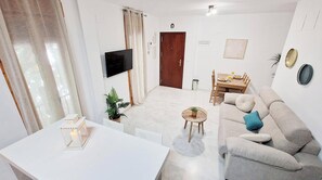 A modern living room with a flat-screen TV, a dining area with a table and chairs, a sofa with cushions, and a small side table with a plant. - Las vides de moriles (Cordoba)
