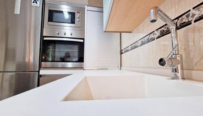 A modern kitchen with stainless steel appliances, a white countertop, and a tiled backsplash. - Las vides de moriles (Cordoba)