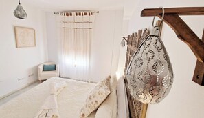 A bedroom with a bed, a chair, a hanging light fixture, and a wall-mounted decorative item. - Las vides de moriles (Cordoba)