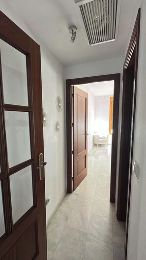 A hallway with a door leading to a room, a ceiling vent, and a light fixture. - Las vides de moriles (Cordoba)