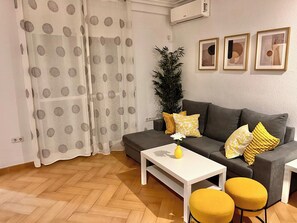A living room with a sofa, a coffee table, two yellow ottomans, a potted plant, and a set of curtains. - Impresionante Puente Romano de Córdoba & Parking (Cordoba)