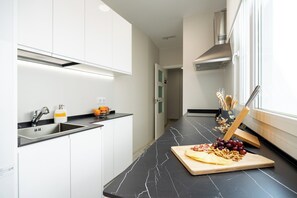 Une cuisine moderne avec des meubles blancs, un plan de travail en marbre noir et une planche à découper en bois sur laquelle sont disposés du fromage et des fruits.