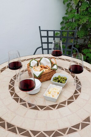 Une table ronde ornée d’un motif géométrique en mosaïque, entourée de quatre verres à vin, d’un panier de pain, d’un bol d’olives et d’une petite assiette de fromage.