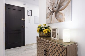 Un couloir avec une porte sombre, une œuvre d’art encadrée au-dessus, et un meuble décoratif orné de motifs.