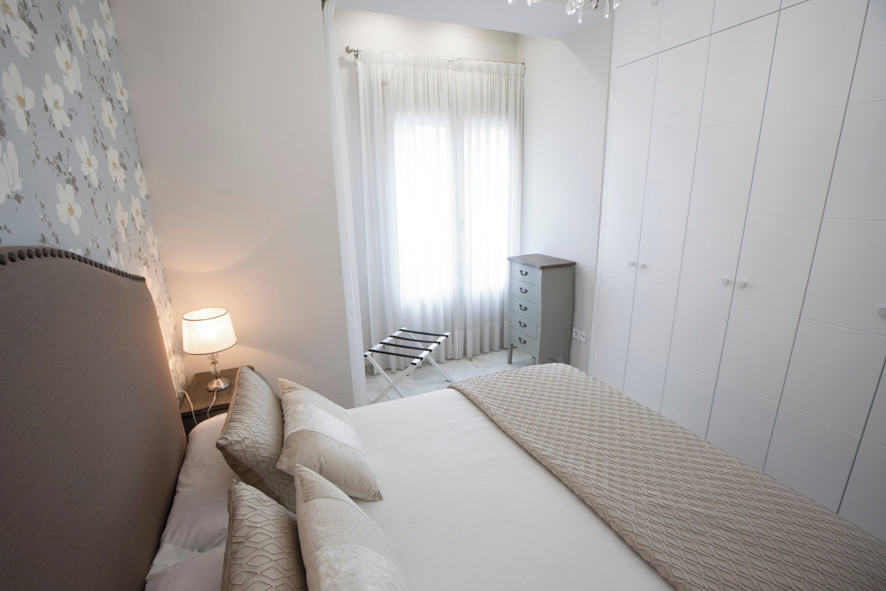 Ein Hotelzimmer mit einem Bett, einem Nachttisch mit Lampe, einem Kleiderschrank und einem Fenster mit Vorhängen.
