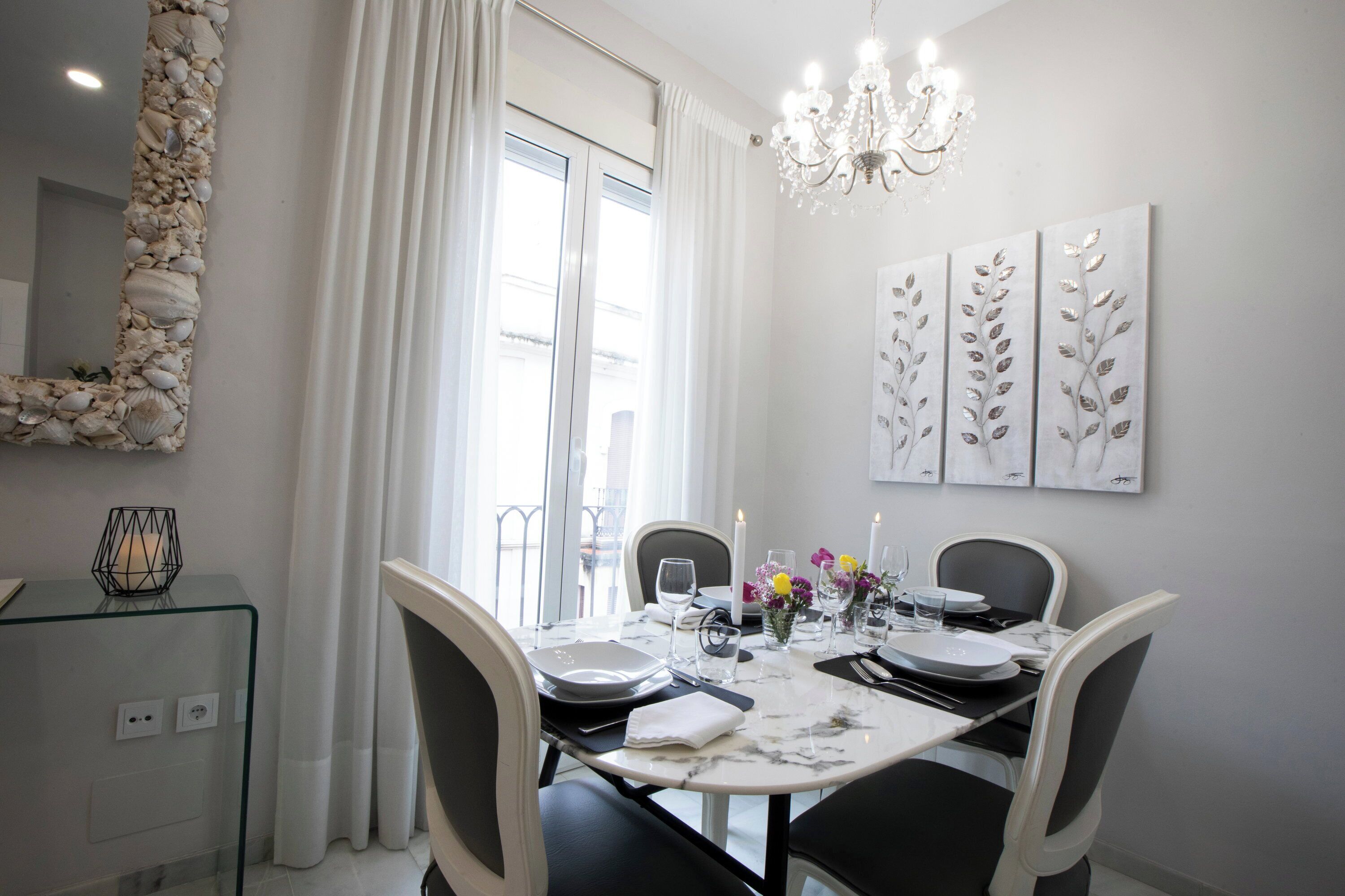 A dining area with a table set for four, a chandelier, and a wall with leaf-patterned artwork.