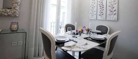 A dining area with a table set for four, a chandelier, and a wall with leaf-patterned artwork.