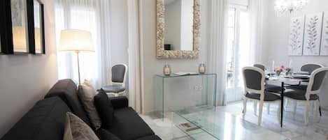 A modern living room with a glass coffee table, a sofa, and a dining area with chairs and a table.
