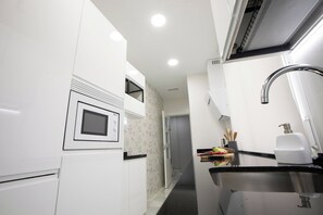 Une cuisine moderne avec des meubles blancs, un four à micro-ondes encastré, un évier en acier inoxydable et une fenêtre au-dessus du plan de travail.