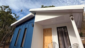 Ein modernes Haus mit blau-weißer Fassade, einer Holztür und zwei Korbstühlen davor.