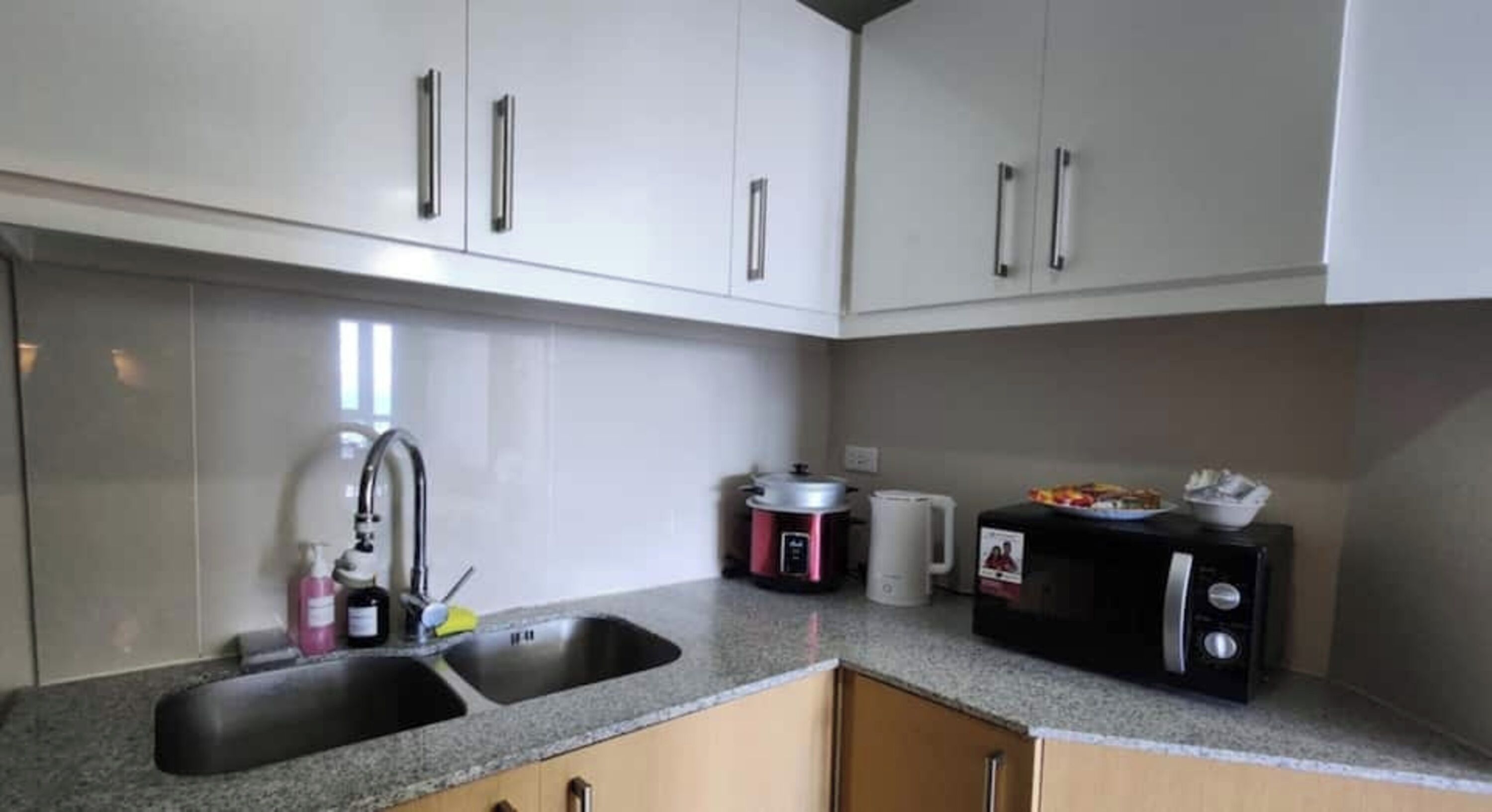 Una cocina con encimera de granito, pileta de acero inoxidable, muebles blancos, microondas y cafetera.