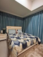 Un dormitorio con cama, mesita de noche y ventana con cortinas.