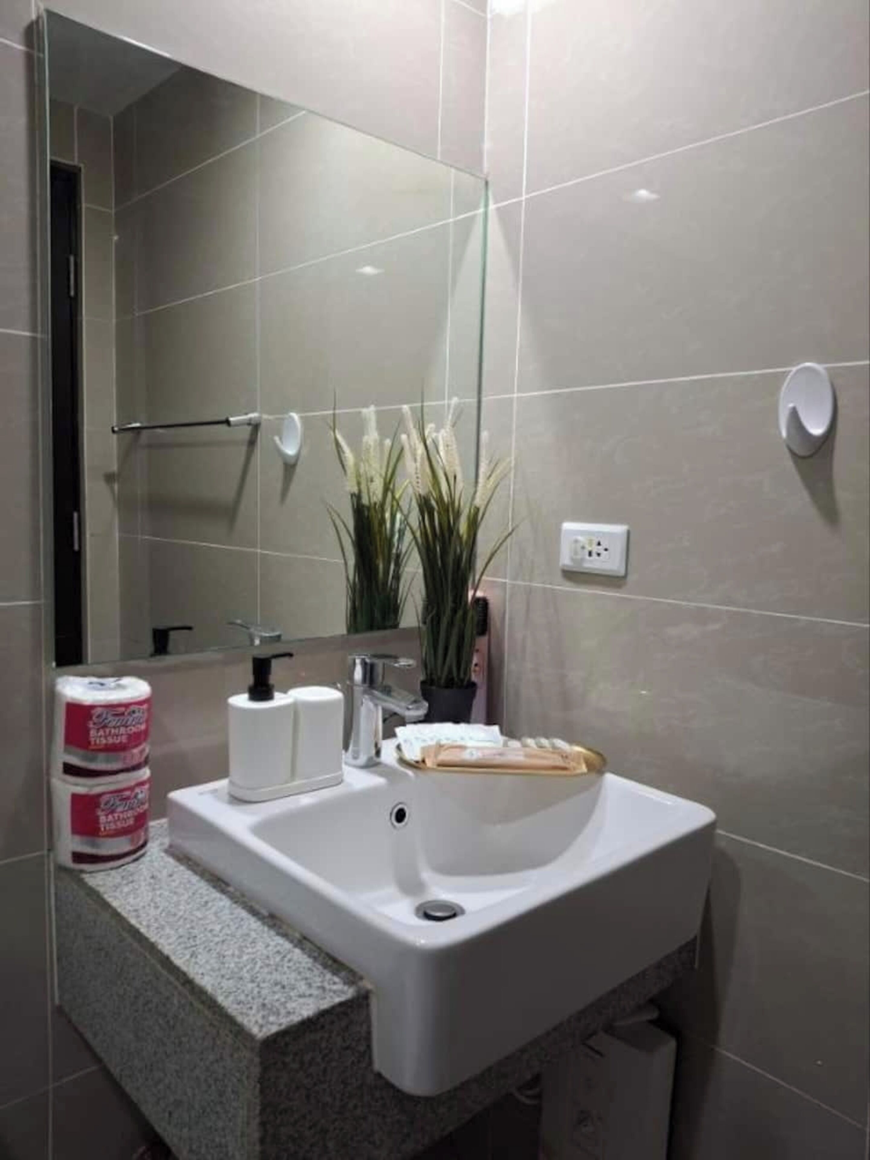 Un baño con un lavamanos blanco, un espejo, un perchero para toallas y una planta en maceta.