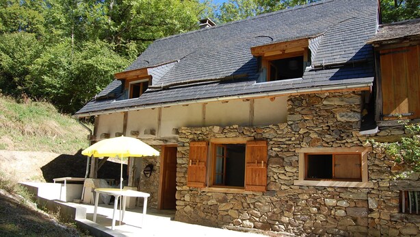 Una casa de piedra con techo inclinado, contraventanas de madera y un ventanal pequeño.