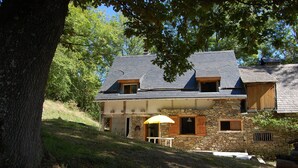 Una casa de piedra con techo inclinado, un pequeño porche y una mesa con sombrilla.