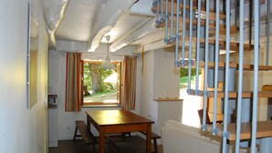 Una habitación con una mesa de madera, bancos, una ventana con cortinas y una escalera con barandillas de metal.