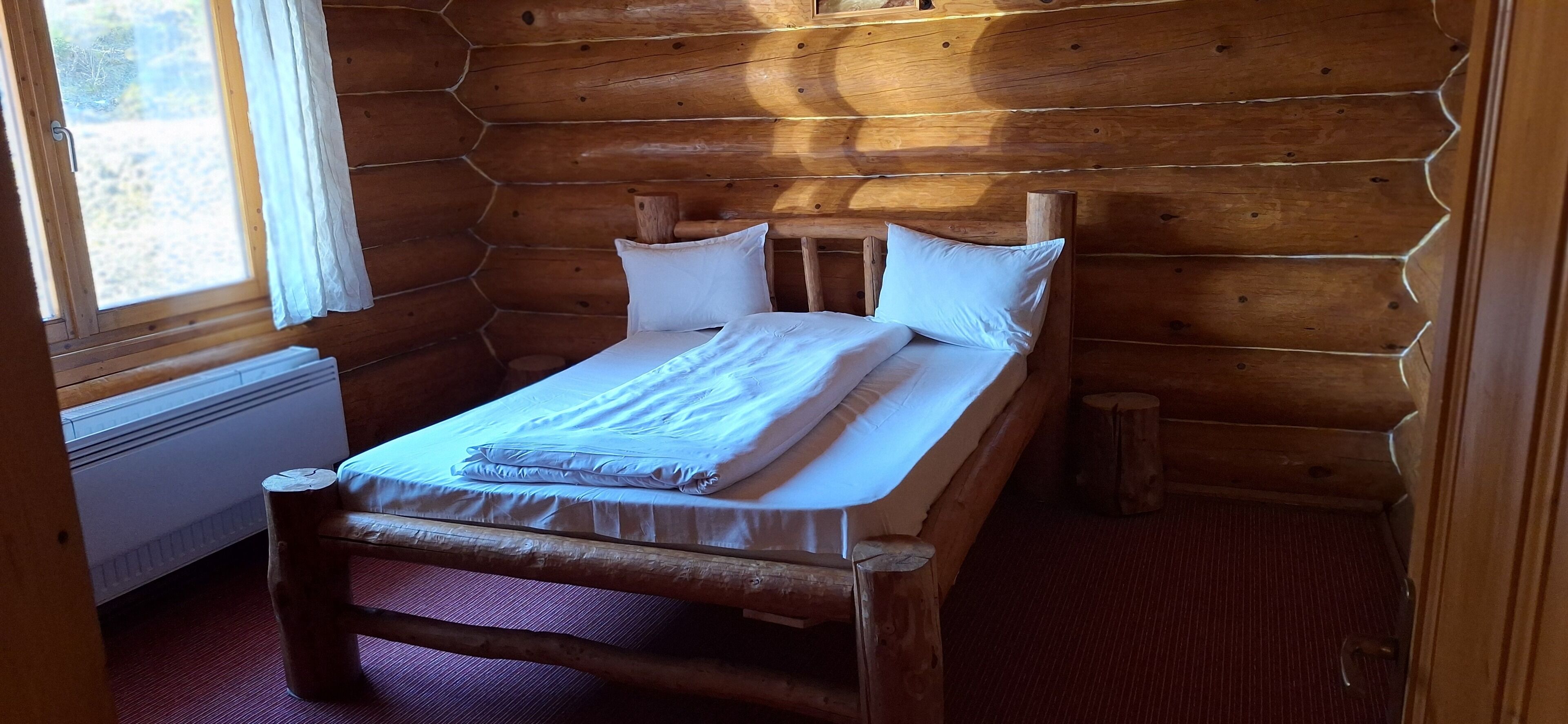 A wooden cabin room with a bed, a window, and a radiator.