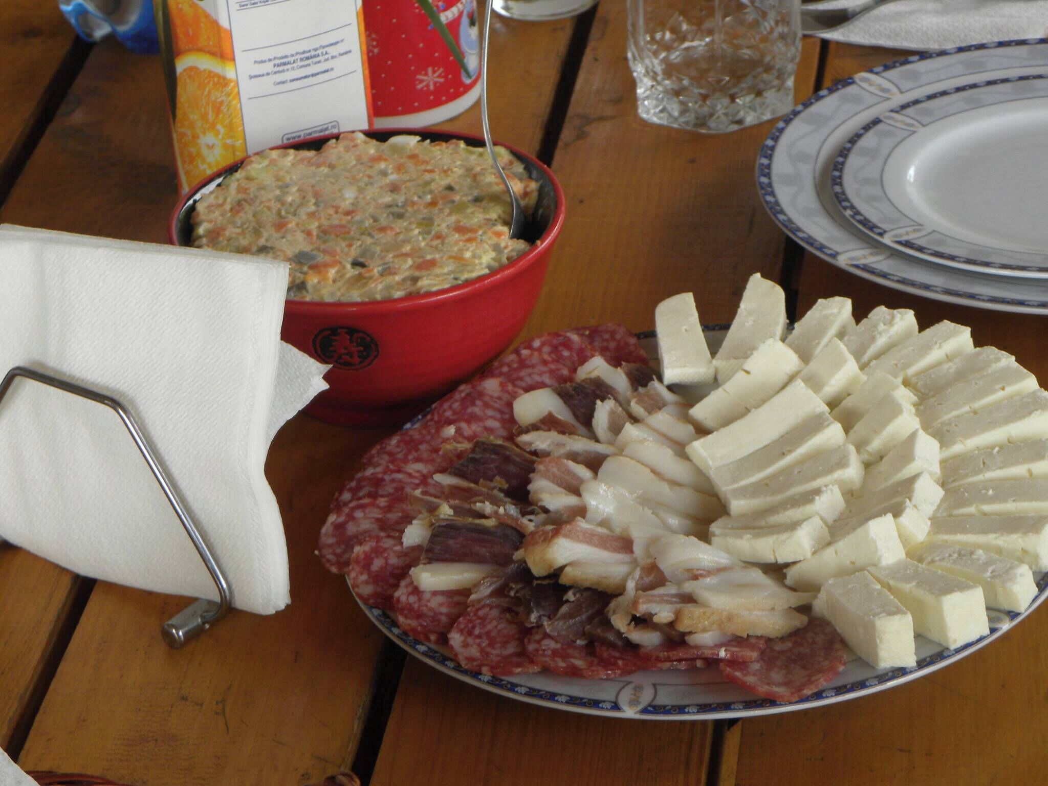 Une table avec une assiette de charcuterie tranchée, un saladier rempli de salade et un bol rouge orné d’un logo.